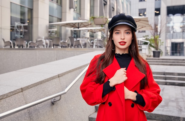 Bella ragazza con un cappotto rosso e un cappello nero per strada