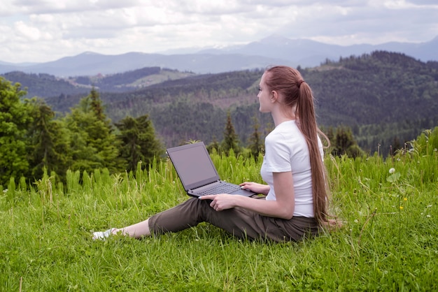 Bella ragazza con un computer portatile che si siede sull'erba verde