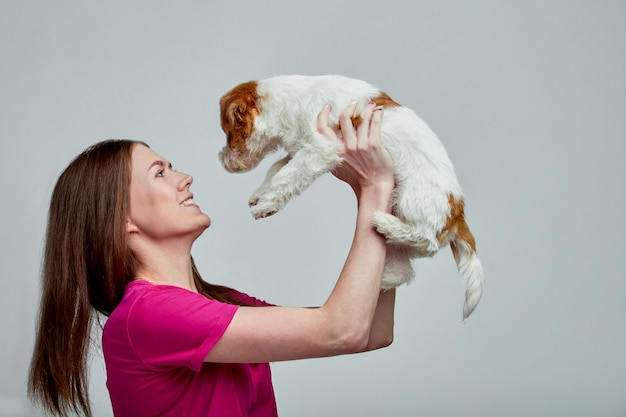 Bella ragazza con un jack russell più terrier sulle sue mani su uno sfondo grigio, copia spazio