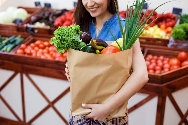 Bella ragazza con un sacco di carta con lo shopping in un negozio di verdure