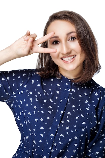 Bella ragazza con un sorriso guardando la telecamera con la mano con due dita su sfondo bianco. Emozioni, espressioni facciali espressive