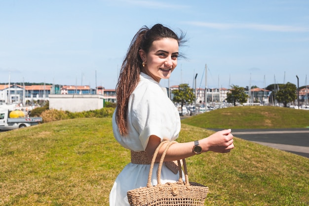 Bella ragazza con un vestito bianco e un cesto che cammina per un villaggio sulla costa