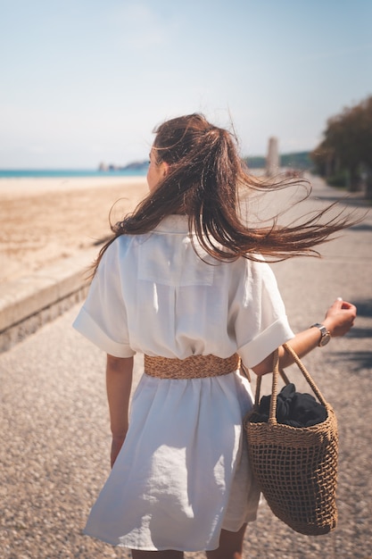 Bella ragazza con un vestito bianco e una borsa che cammina attraverso un villaggio della costa