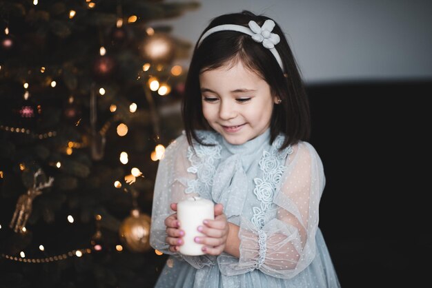 Bella ragazza con una candela accesa in posa su un albero decorato di Natale