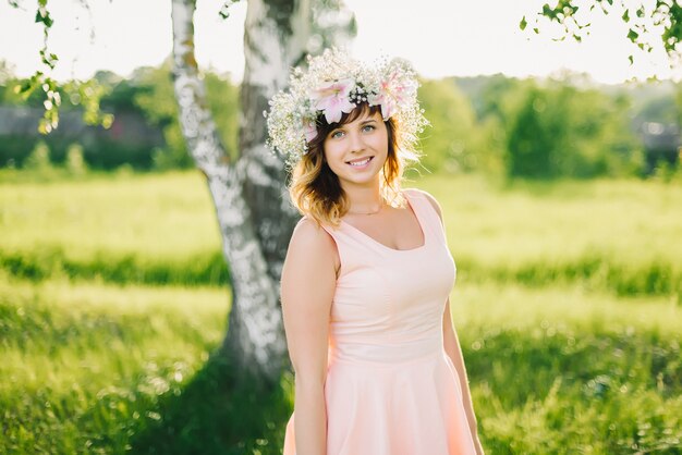 Bella ragazza con una corona di fiori sulla sua testa che sorride all'aperto in una giornata di sole