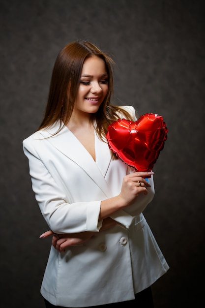 Bella ragazza con una giacca bianca con un cuore a palloncino rosso tra le mani