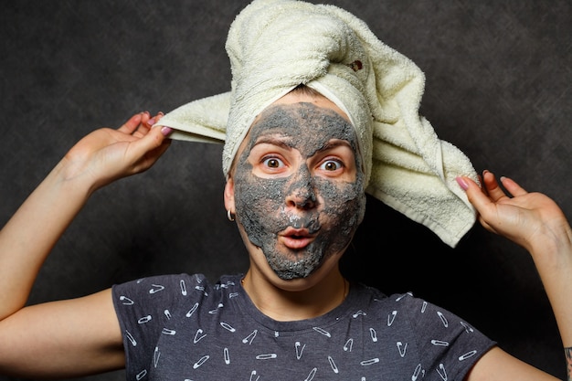 Bella ragazza con una maschera tonica in schiuma sul viso e un asciugamano legato con i capelli