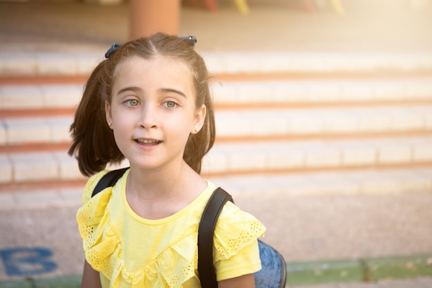 Bella ragazza dagli occhi chiari con due trecce e il suo zaino, è felice di tornare a scuola.