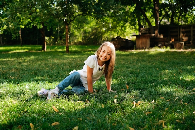 bella ragazza dai capelli biondi di 9 anni si siede nel lussureggiante parco estivo di gpzon di erba verde