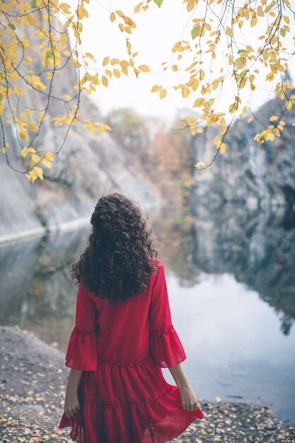 Bella ragazza dai capelli ricci con un vestito rosso al lago che guarda lontano dalla telecamera