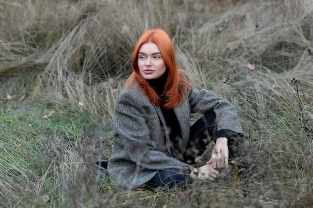 Bella ragazza dai capelli rossi attiva che cammina nel bosco. Autoisolamento all'aria aperta. La ragazza seduta da sola nella foresta verde gode del silenzio e della bellezza della natura.