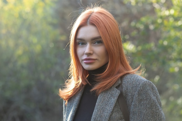 Bella ragazza dai capelli rossi attiva che cammina nel bosco. donna in abito nero nel bosco guardando la telecamera