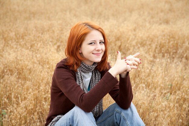 Bella ragazza dai capelli rossi che si siede all'erba gialla di autunno.