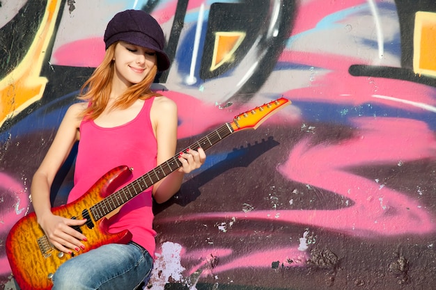 Bella ragazza dai capelli rossi con chitarra e muro di graffiti