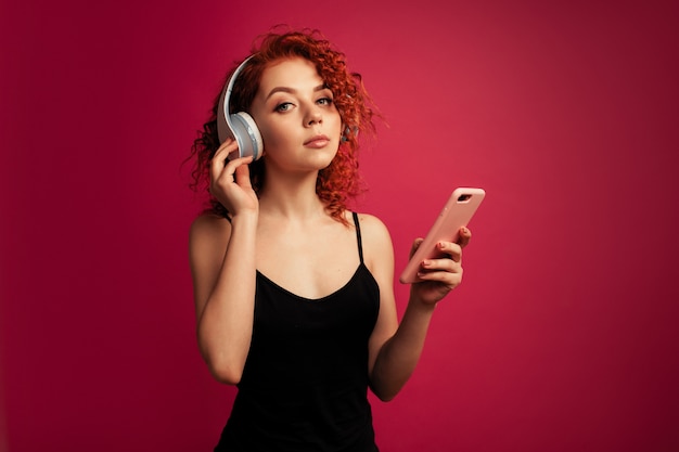 Bella ragazza dai capelli rossi in grandi cuffie bianche con il telefono in mano l&#39;ascolto di musica