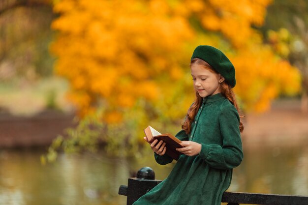 bella ragazza dai capelli rossi in un vestito verde e fare una passeggiata in autunno nel parco con un libro