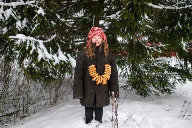 Bella ragazza del villaggio si trova nella foresta di neve con involtini secchi a forma di anello e sorrisi in inverno