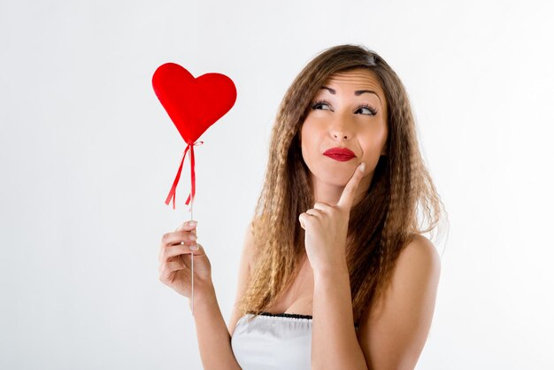 Bella ragazza di pensiero in piedi e in possesso di cuore rosso.