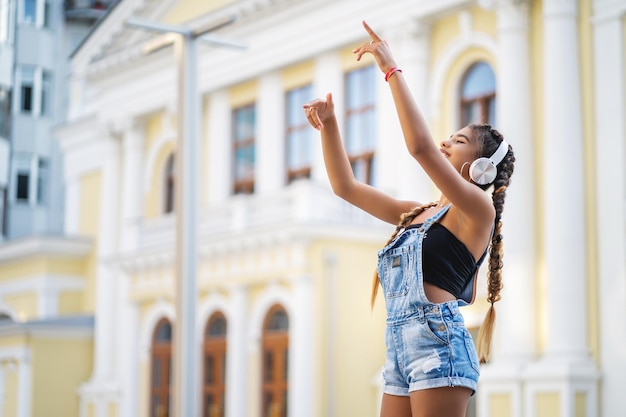 Bella ragazza di razza mista che ascolta musica in cuffia e balla con le braccia alzate