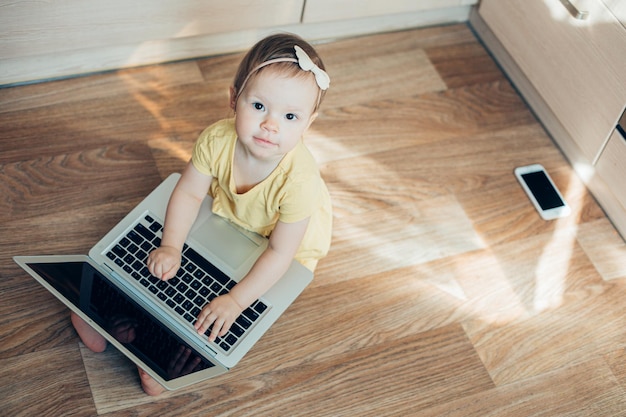 Bella ragazza di un anno seduta sul pavimento con un computer portatile e sorridente