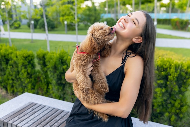 Bella ragazza e il suo piccolo cane barboncino dorato passeggiano nel parco pubblico all'aperto