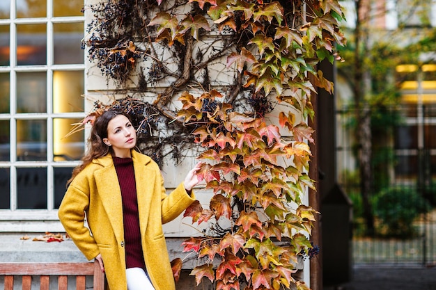 Bella ragazza elegante con un cappotto giallo cammina per le strade di Parigi