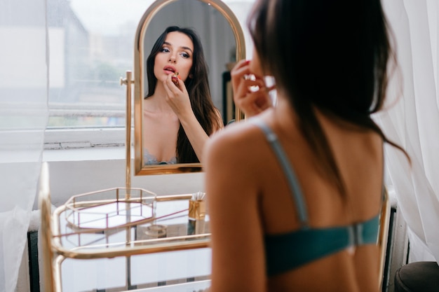 Bella ragazza elegante in biancheria intima che fa trucco alla toletta