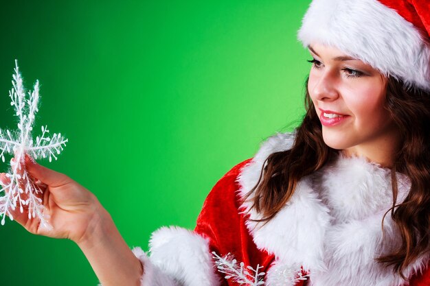 Bella ragazza emotiva con i capelli lunghi vestita da Babbo Natale in posa su uno sfondo verde cromato