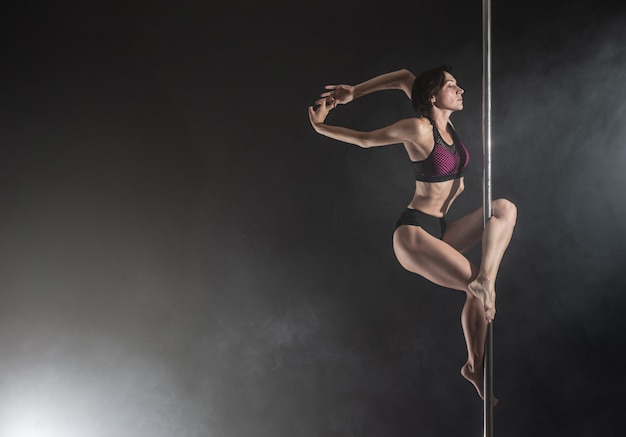 Bella ragazza esile con pilone. Ballerino femminile del palo che balla sul nero