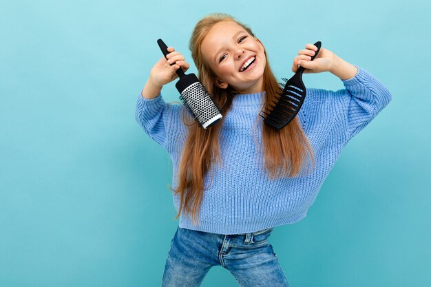 Bella ragazza europea che pettina i suoi capelli su blu-chiaro