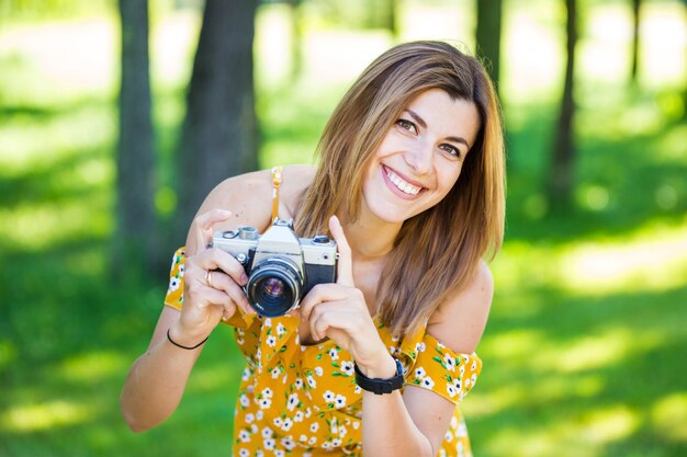 Bella ragazza europea in un vestito giallo con una retro macchina fotografica nel parco di mattina