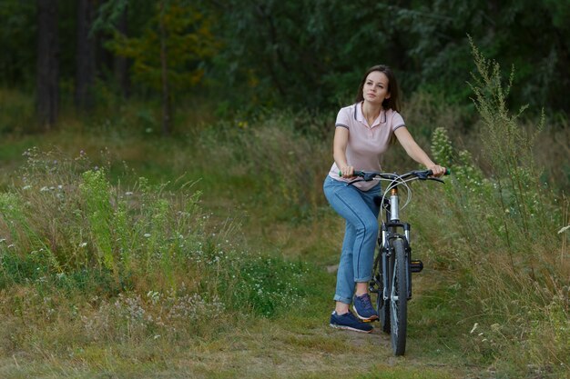 Bella ragazza felice che guida in bicicletta nella foresta