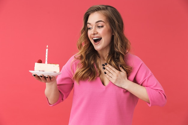 Bella ragazza felice che indossa abiti casual in piedi isolata sul muro rosa, festeggia il compleanno con la torta