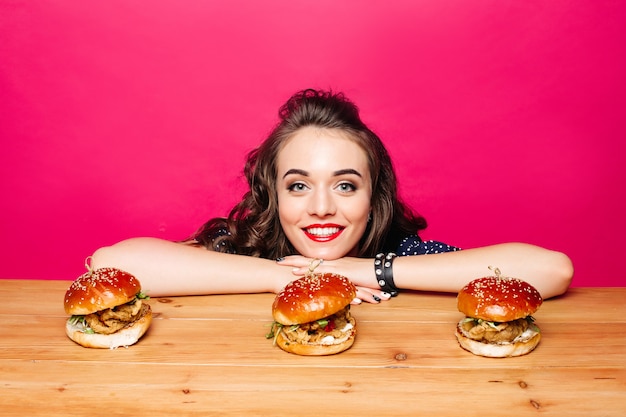 Bella ragazza felice con l'acconciatura con tre hamburger su di legno