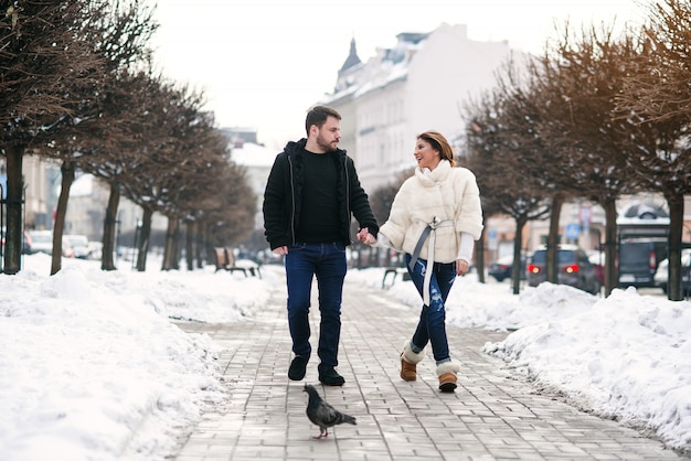 Bella ragazza felice e il suo bel ragazzo che camminano insieme sulla strada innevata d'inverno. Capodanno e Natale.