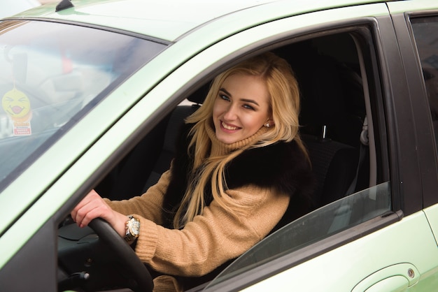 Bella ragazza felice sul finestrino della macchina, giovane donna alla guida della sua auto