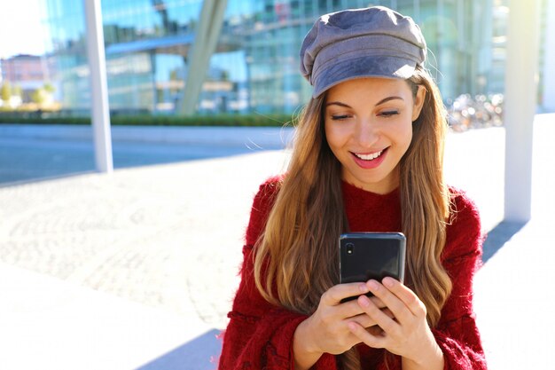 Bella ragazza felice utilizzando smart phone nella città moderna. Ritratto di ragazza moda autunno inverno.