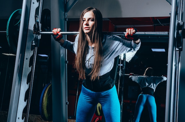 Bella ragazza fitness si trova vicino al bilanciere nel moderno centro fitness