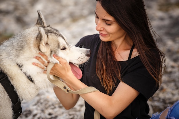 Bella ragazza gioca con un cane, husky grigio e bianco, in montagna al tramonto. Ragazza indiana e il suo lupo