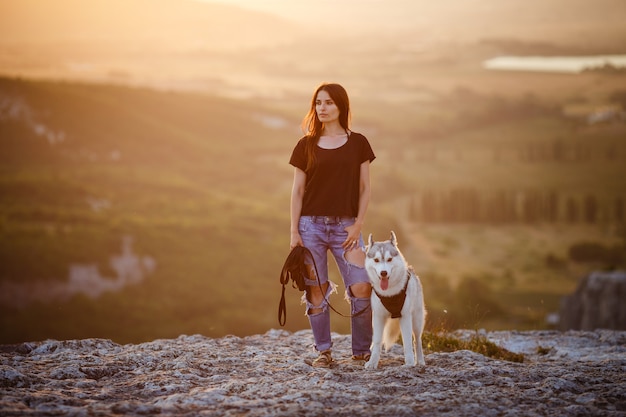 Bella ragazza gioca con un cane, husky grigio e bianco, in montagna al tramonto. Ragazza indiana e il suo lupo