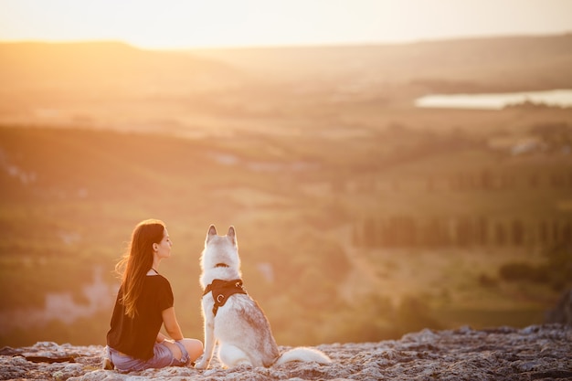 Bella ragazza gioca con un cane, husky grigio e bianco, in montagna al tramonto. Ragazza indiana e il suo lupo