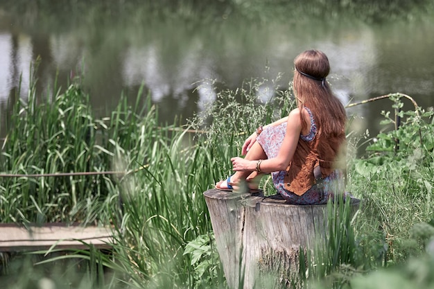 Bella ragazza hippie seduta su un ceppo e guardando lo stagno