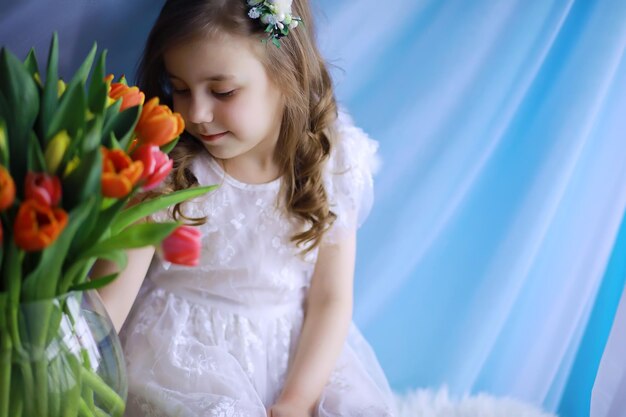 Bella ragazza in abiti bianchi con un magnifico bouquet dei primi tulipani. Giornata internazionale della donna. Ragazza con i tulipani.