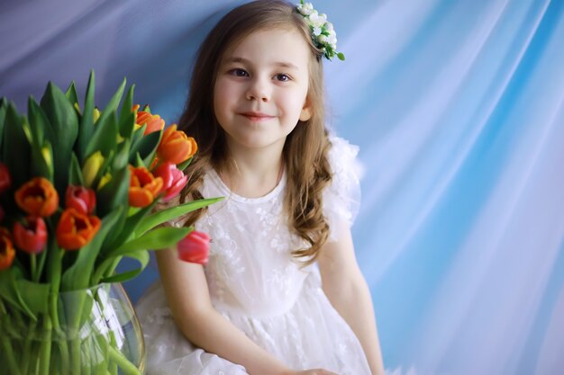 Bella ragazza in abiti bianchi con un magnifico bouquet dei primi tulipani. Giornata internazionale della donna. Ragazza con i tulipani.