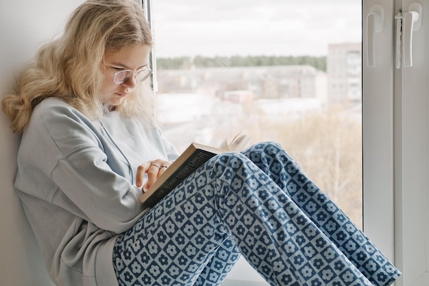 Bella ragazza in abiti casual si siede sul davanzale e legge un libro