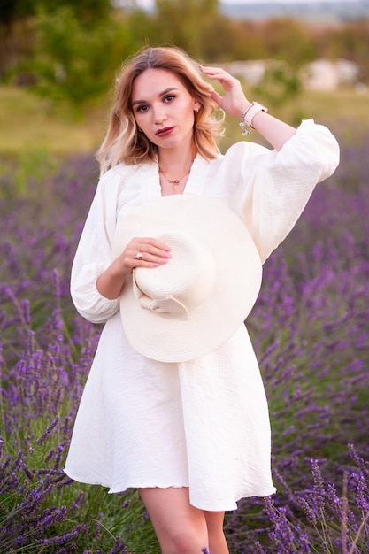 bella ragazza in abito bianco e cappello in un campo di lavanda al tramonto