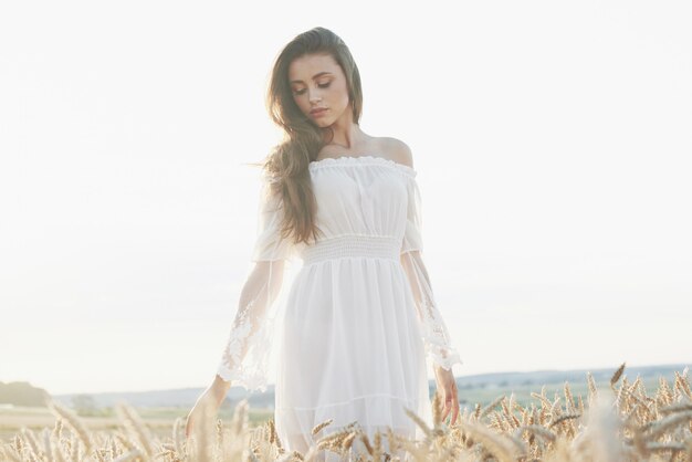 Bella ragazza in abito bianco in esecuzione sul campo di grano in autunno al tramonto