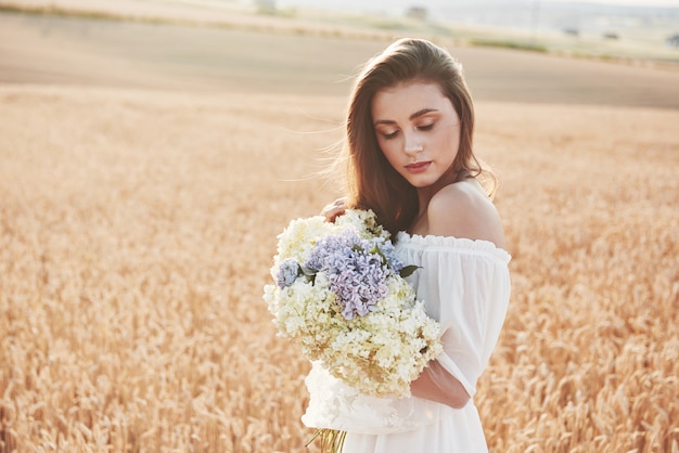 Bella ragazza in abito bianco in esecuzione sul campo di grano in autunno al tramonto.