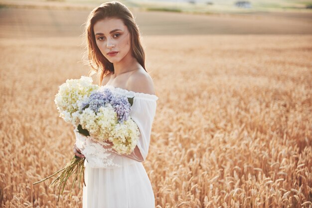 Bella ragazza in abito bianco in esecuzione sul campo di grano in autunno al tramonto.