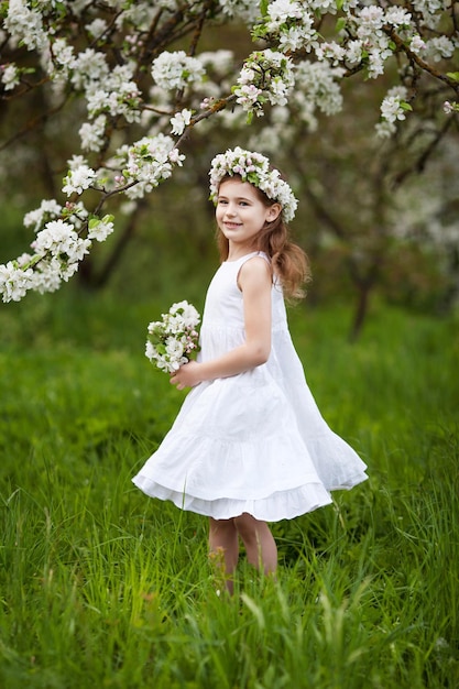 Bella ragazza in abito bianco in giardino con alberi di mele in fiore Ragazza sorridente divertendosi e godendo